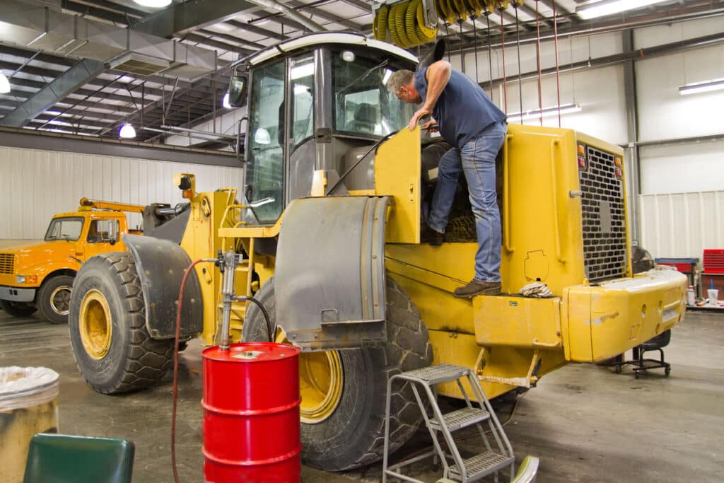 Technician inspecting heavy equipment AC system inside a service bay before summer heat